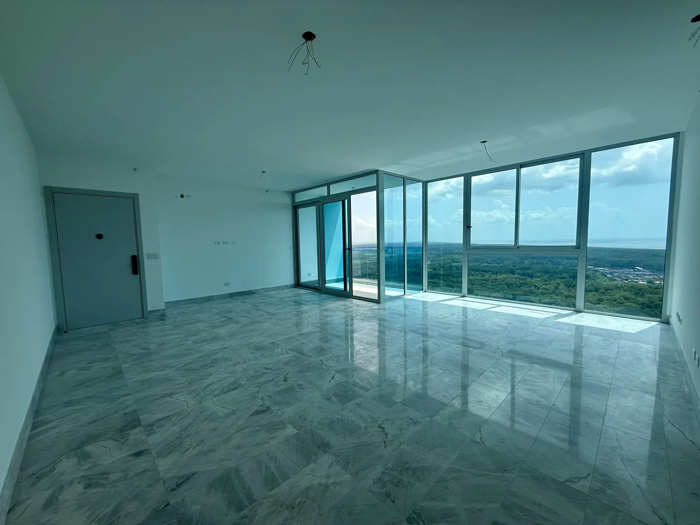 Unfurnished room with marble floors, white walls, and floor-to-ceiling windows overlooking a green landscape and blue sky.