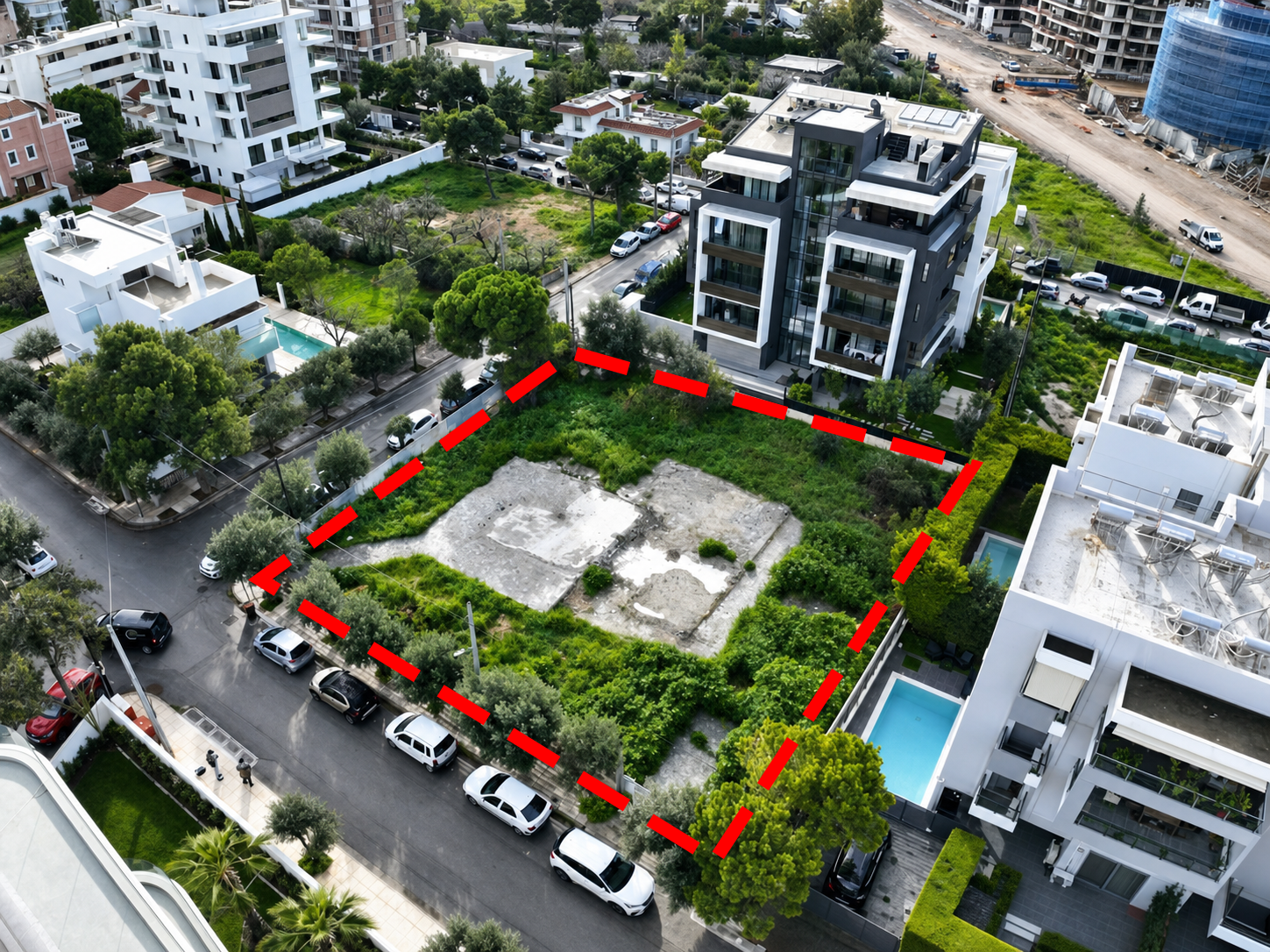 Aerial view of a vacant rectangular lot outlined in red, surrounded by modern apartment buildings and parked cars.