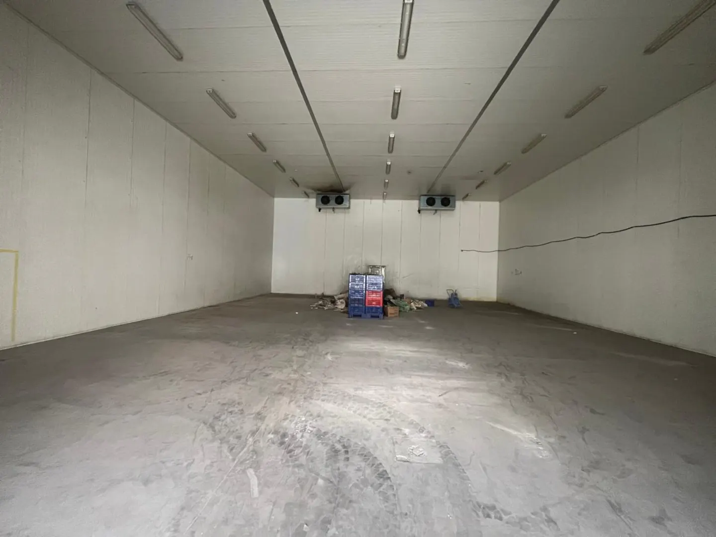 A large, empty white warehouse with a gray concrete floor and fluorescent lighting.