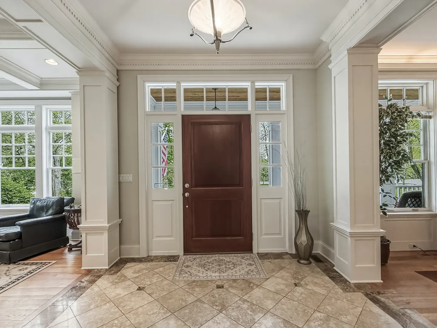 A home's foyer with a dark wood door, white trim, and tile floor. A light fixture hangs from the ceiling.