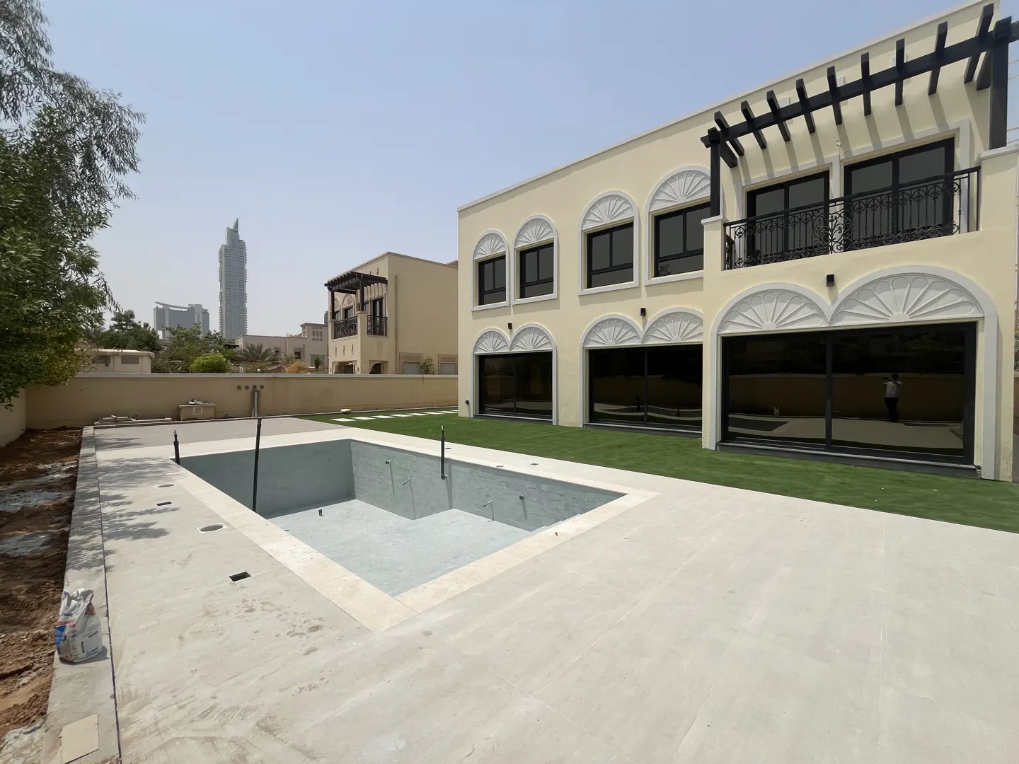 Exterior view of a two-story, light yellow house with a balcony, black windows, and an empty swimming pool in the backyard.