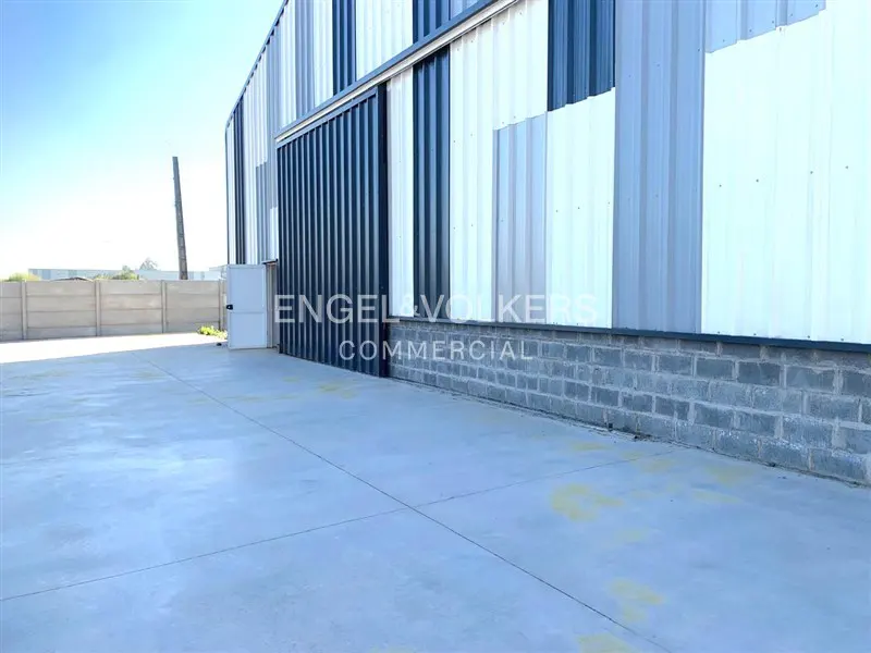 Exterior of a commercial building with blue and white corrugated metal siding and a concrete parking area.