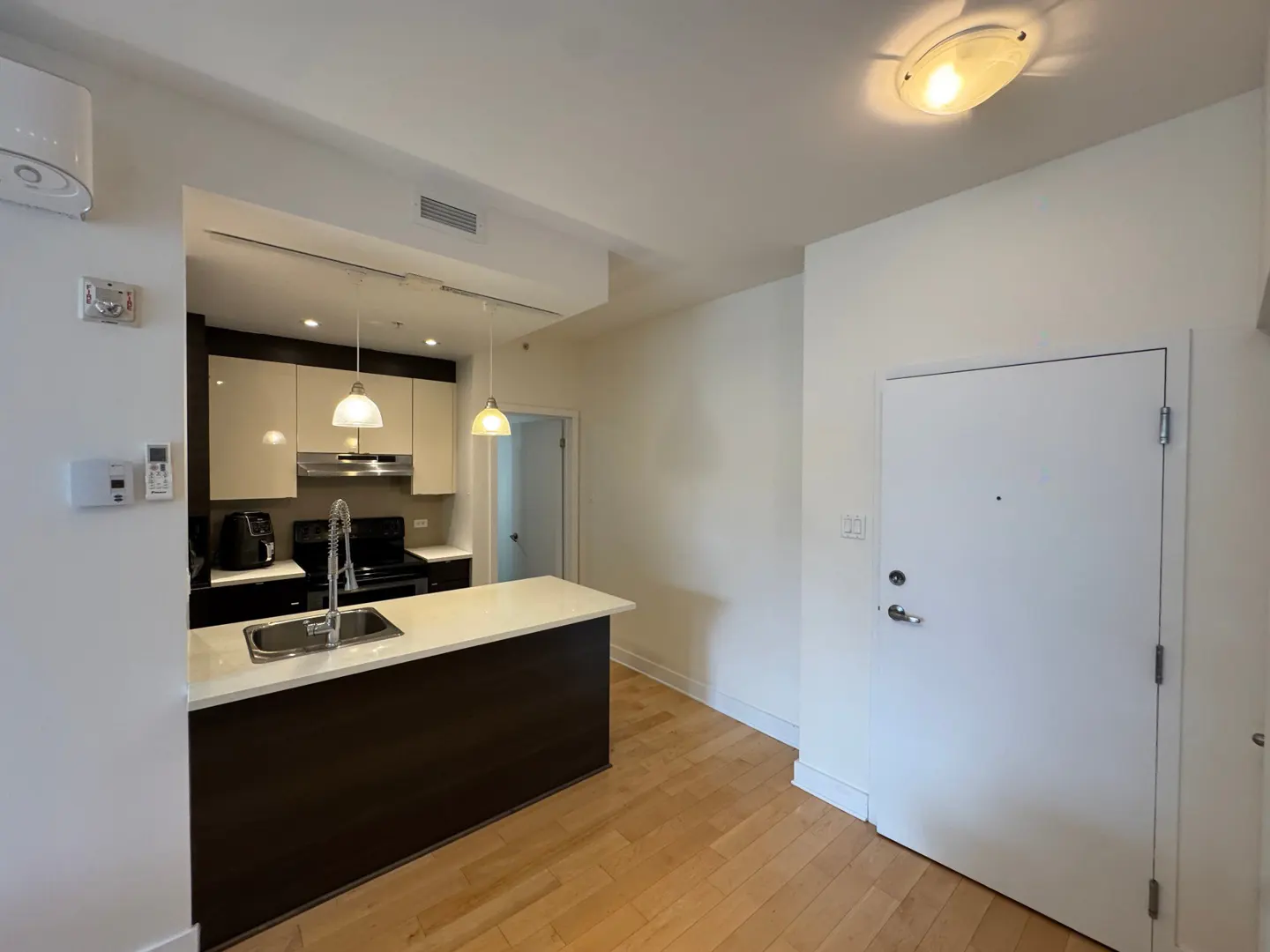 A modern kitchen with a dark brown island, white countertops, and stainless steel sink. Hardwood floors and a white door are visible.