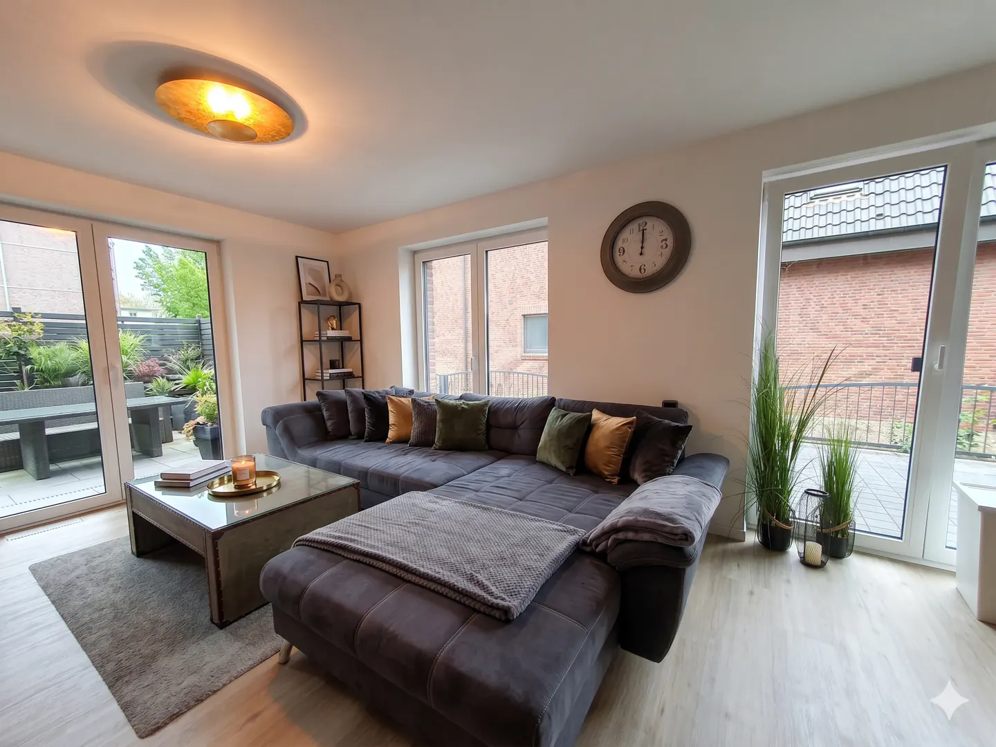 Living room with a large gray sectional sofa, a glass coffee table, and a view of the outdoor patio through sliding glass doors.