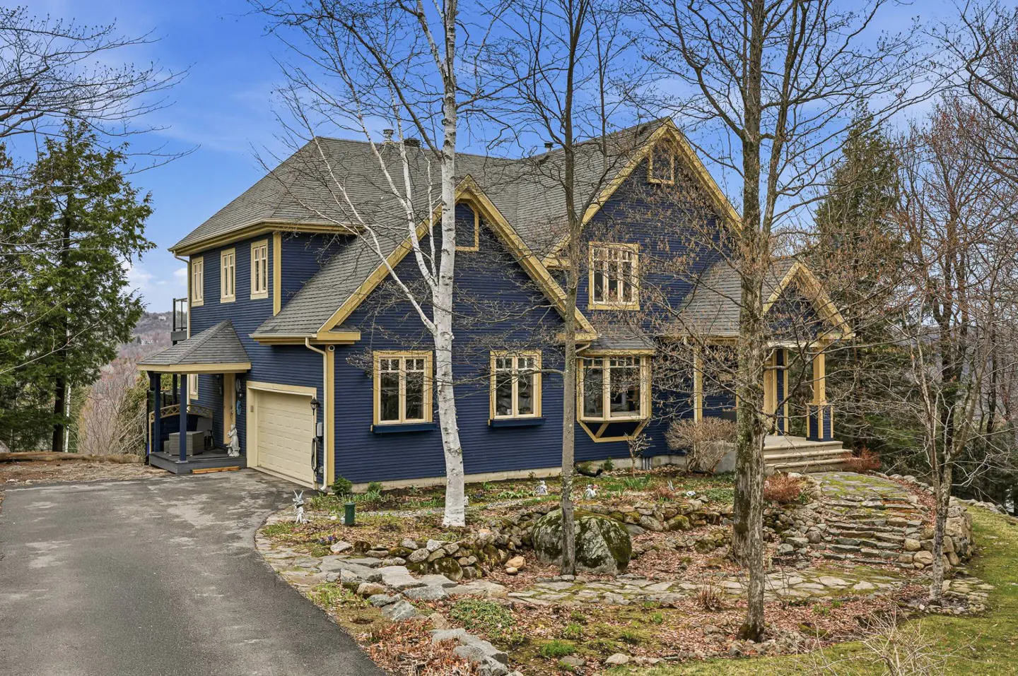 Two-story navy house with tan trim, a gray roof, and a tan garage door, surrounded by trees.