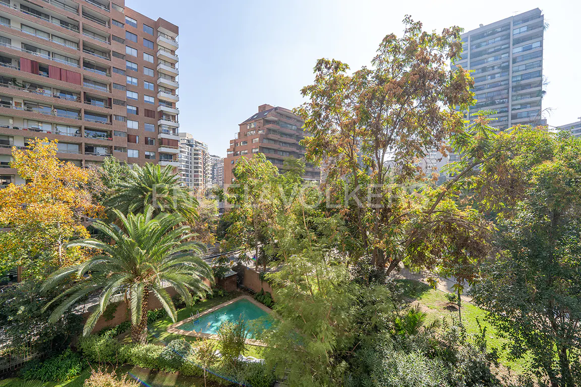 View of a city park with a pool, surrounded by trees and tall apartment buildings.