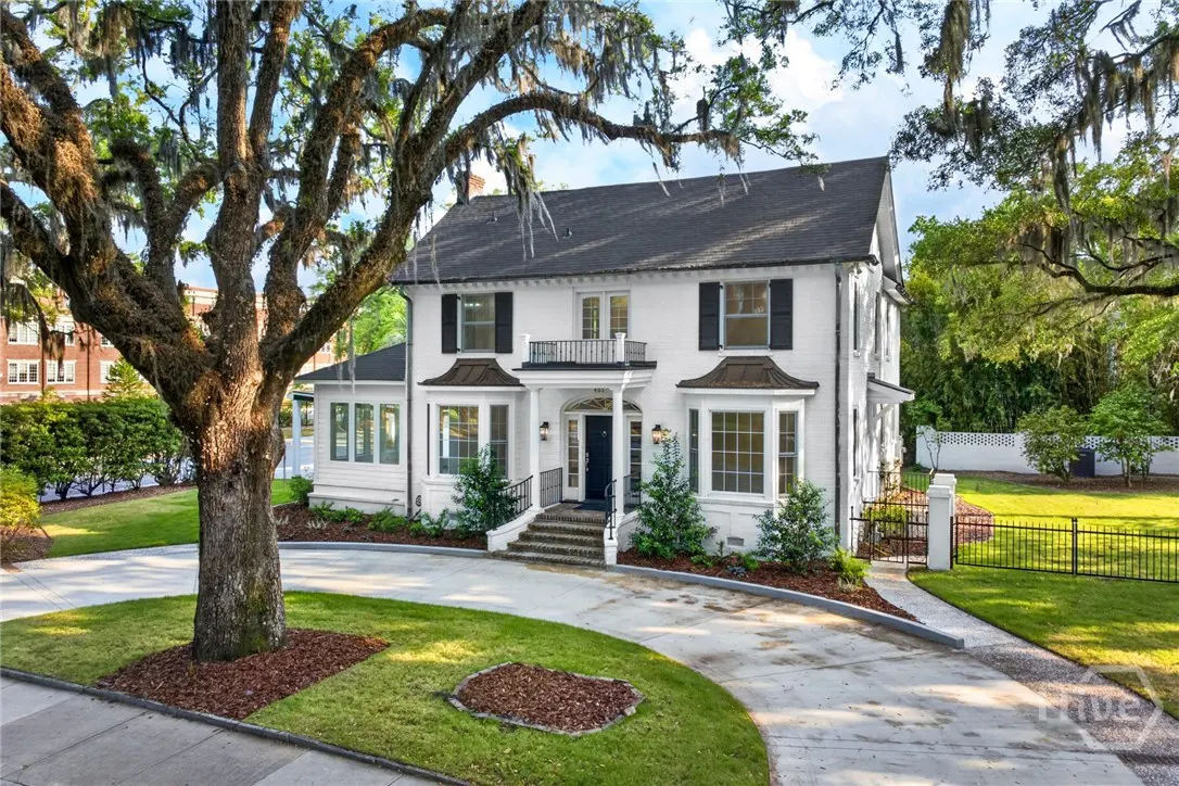Two-story white house with black shutters and a black roof. A large tree with Spanish moss is in the front yard.