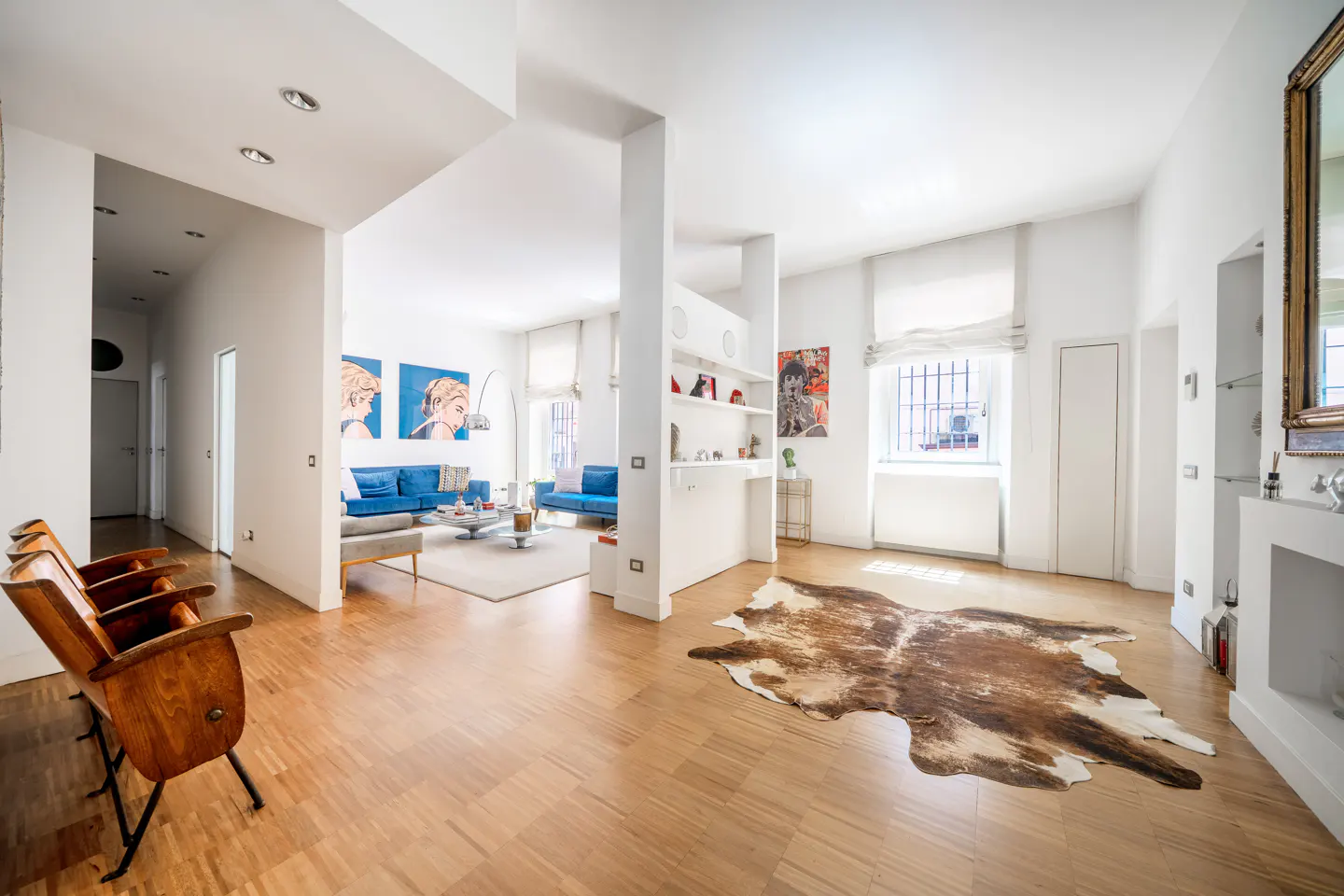 Bright, open-plan living room with hardwood floors, a cowhide rug, vintage wooden theater seats, and blue sofas.