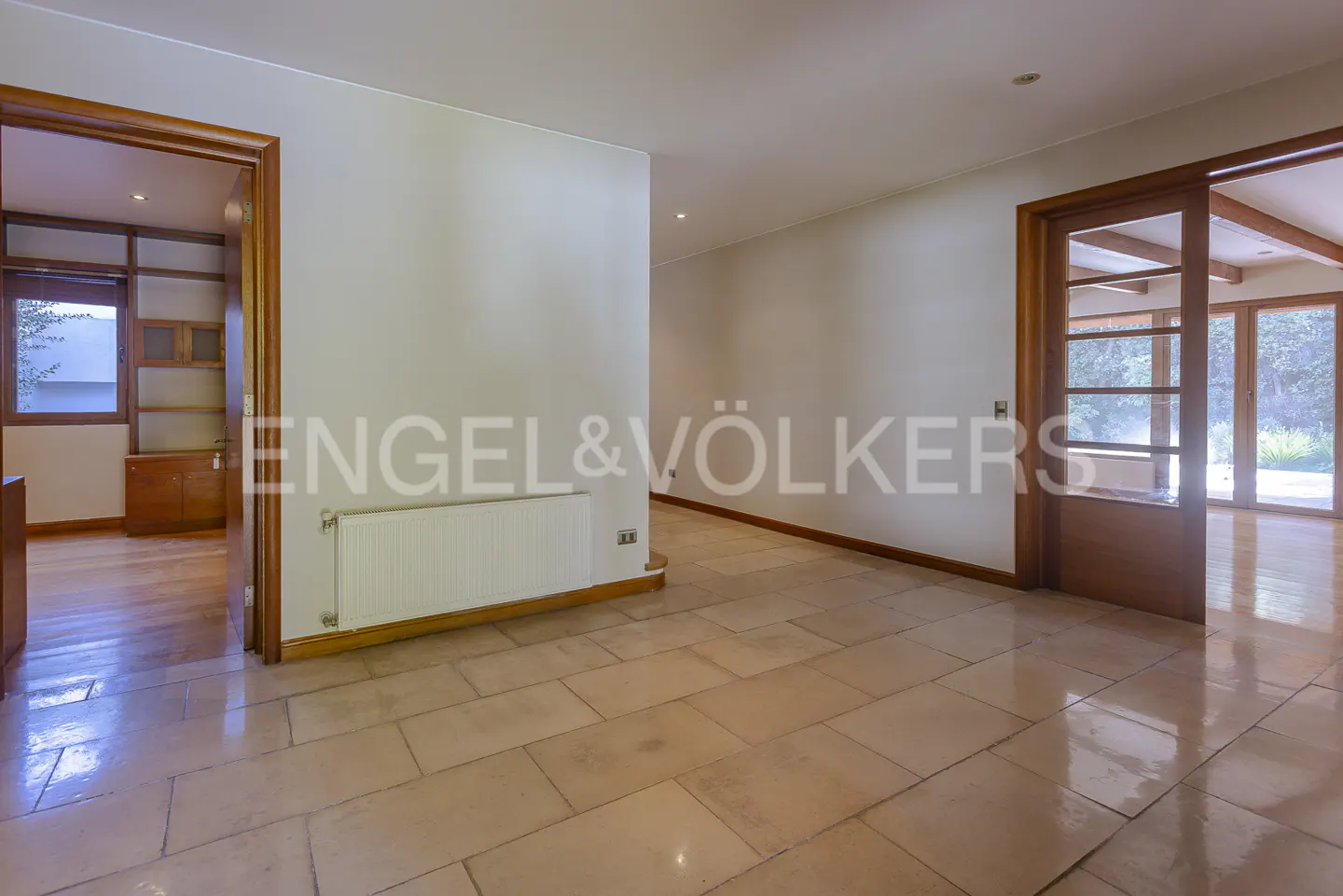 An interior view of a home with beige tile flooring, white walls, and wooden door frames. The Engel & Völkers logo is visible on the wall.