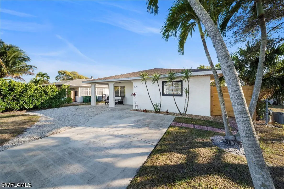 A white single-story house with palm trees, a concrete driveway, and a covered porch on a sunny day.