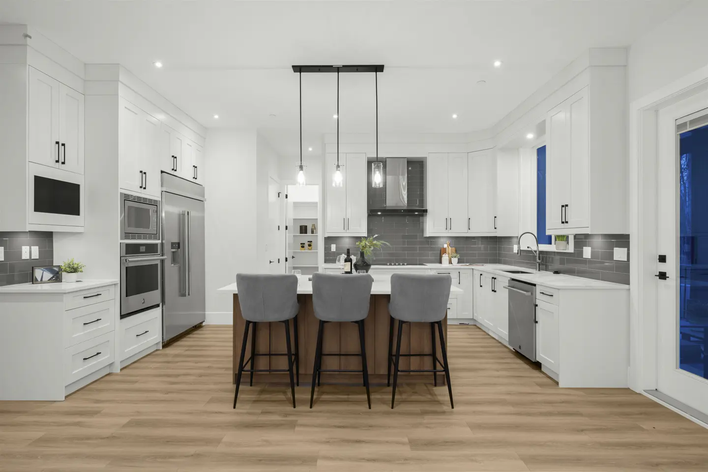 Bright, modern kitchen with white cabinets, stainless steel appliances, and a wood-paneled island with three gray bar stools.