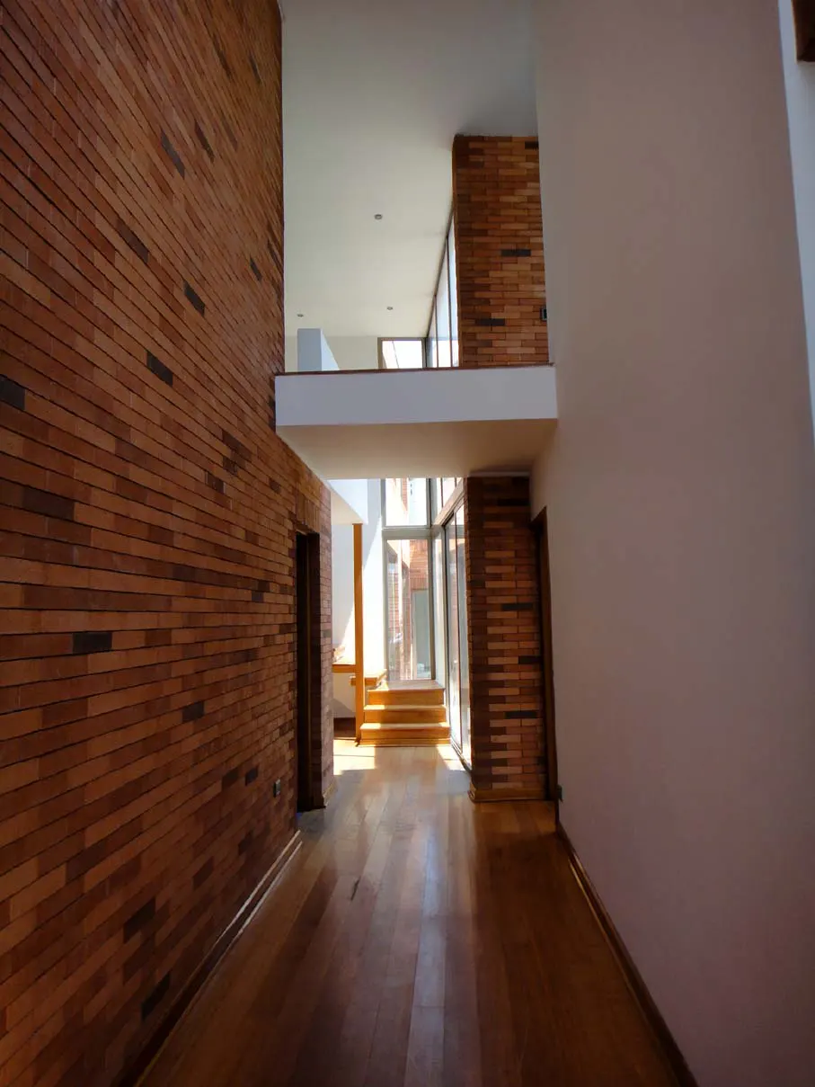 Modern home interior with brick walls, wood floors, and a white balcony overlooking a bright, open space.