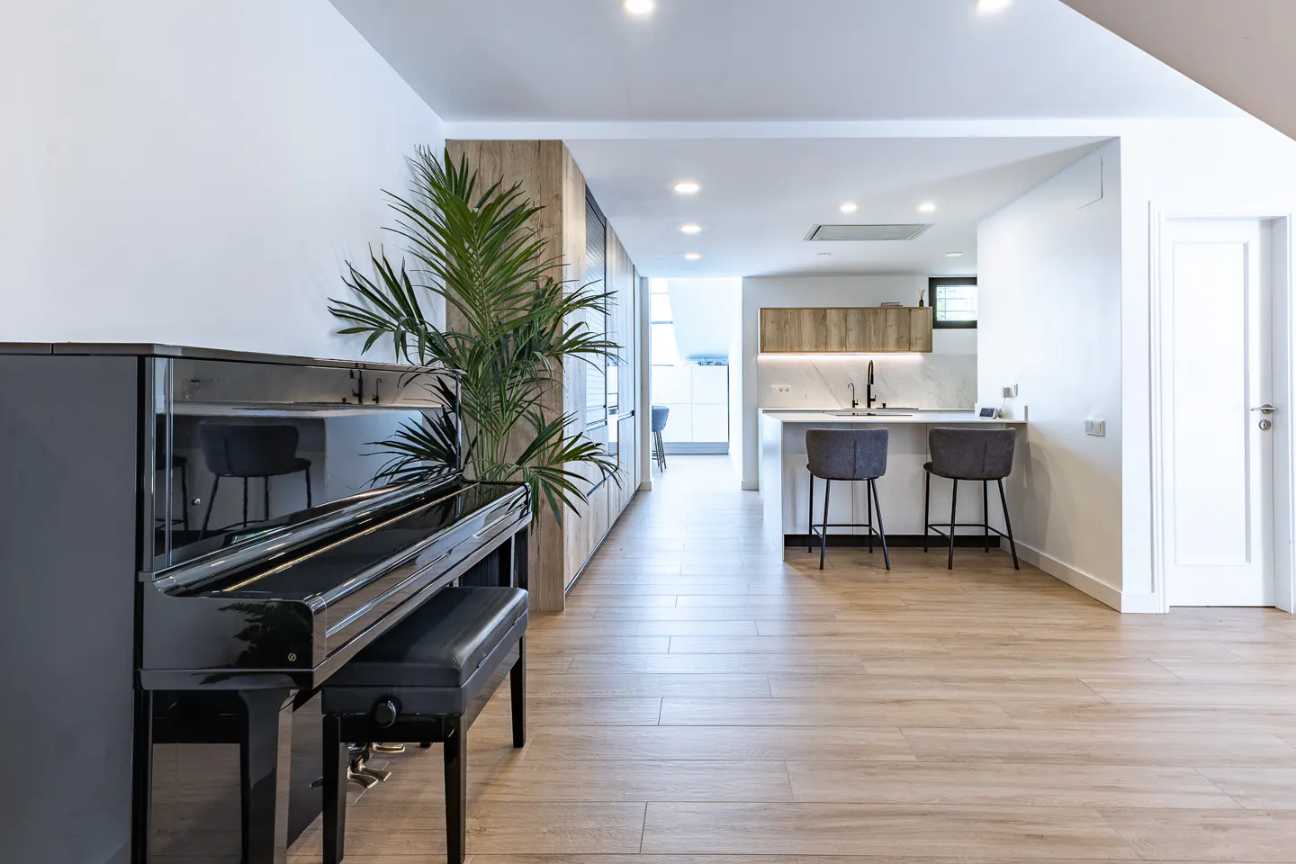 Open-concept living space with a black piano, wood floors, and a kitchen island with gray stools.