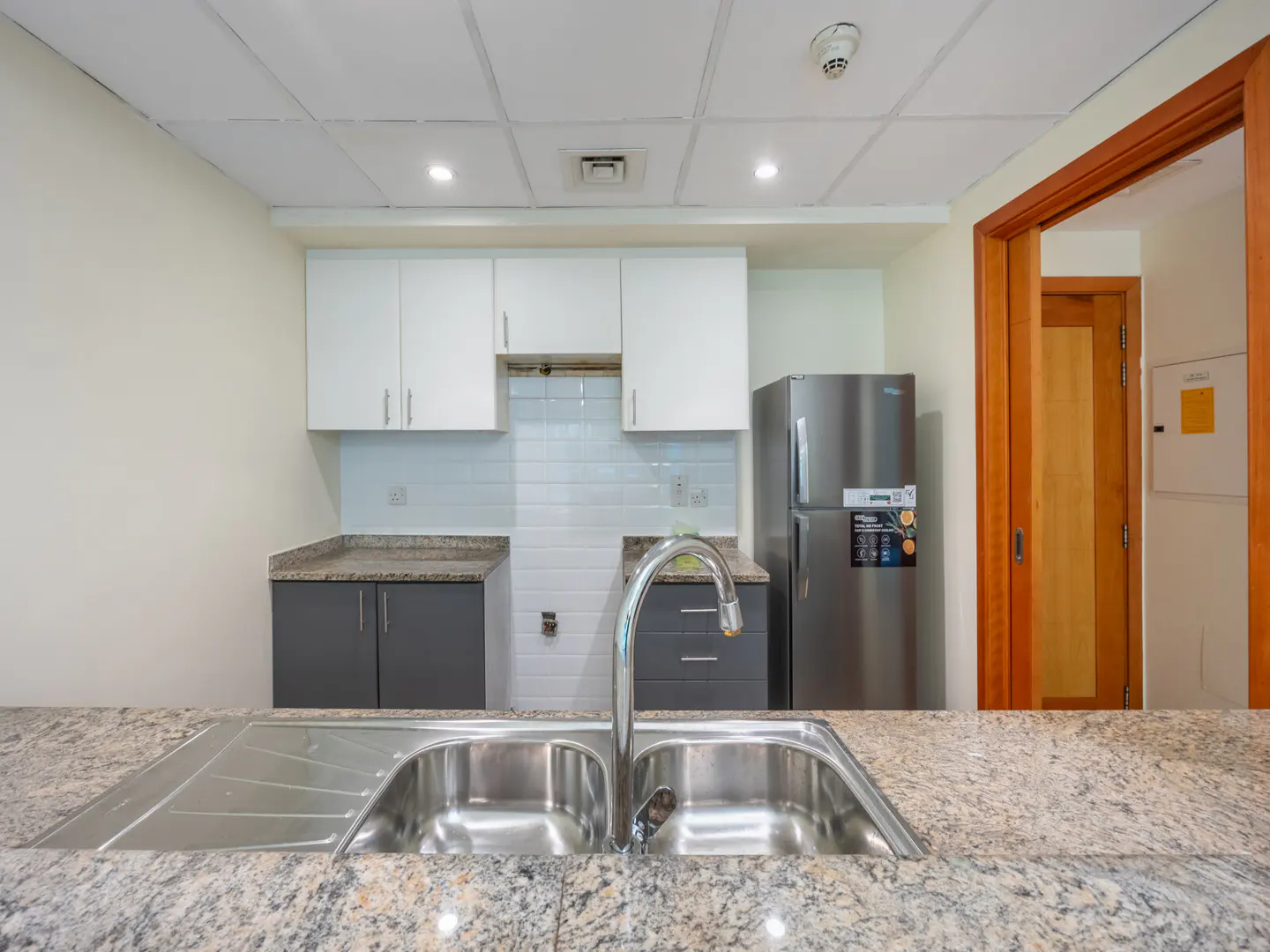 A kitchen with white cabinets, gray lower cabinets, stainless steel fridge, and granite countertops.