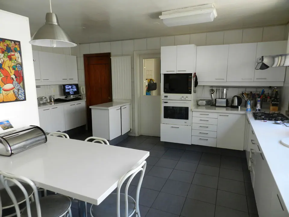 Bright kitchen with white cabinets, gray tile floor, and a white table with chairs. Appliances include a microwave and oven.