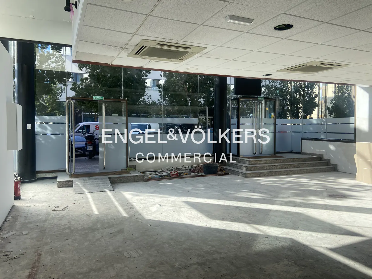 Engel & Völkers commercial space with glass doors and windows. The interior is bright with a white ceiling and concrete floor.