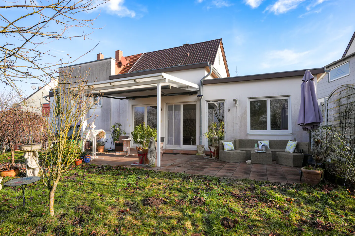 Backyard view of a white house with a patio, furniture, and green lawn under a blue sky.