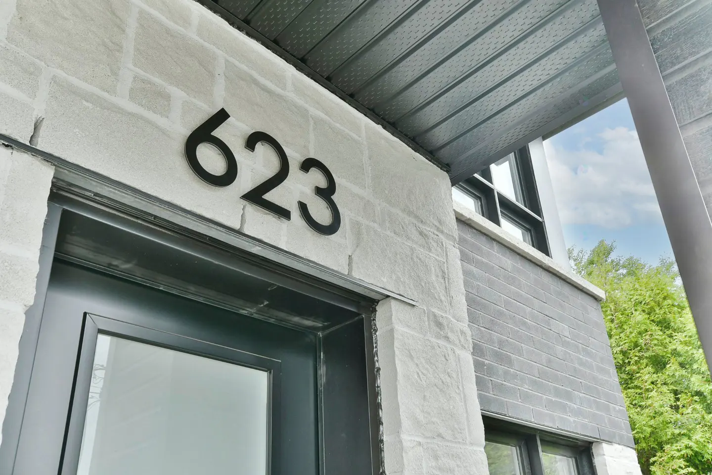 Close-up of a building's exterior with the number "623" in black on a light stone wall above a dark green door.