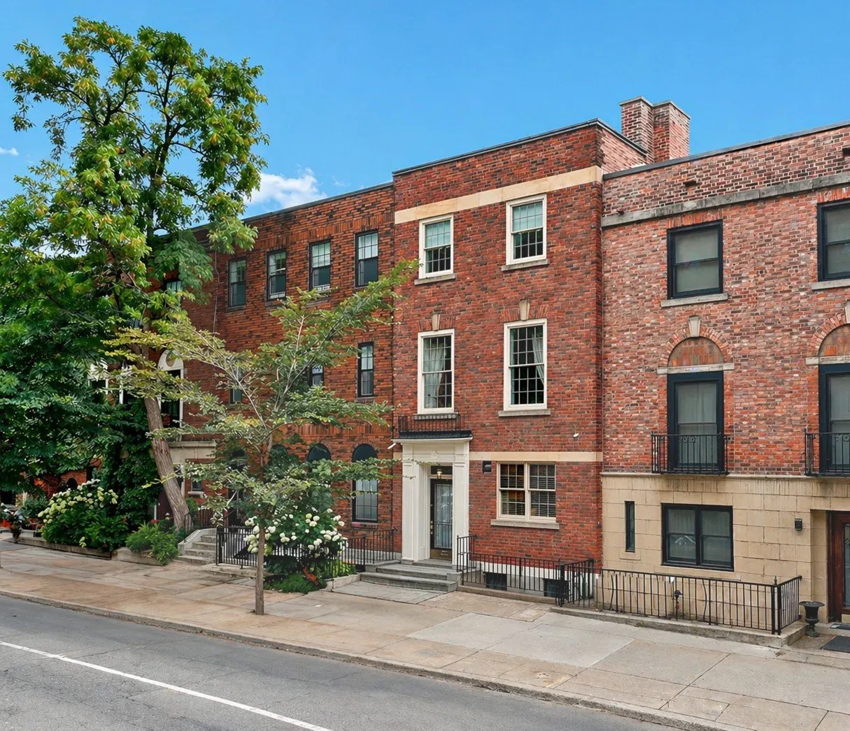 A three-story red brick apartment building with black framed windows and green trees.