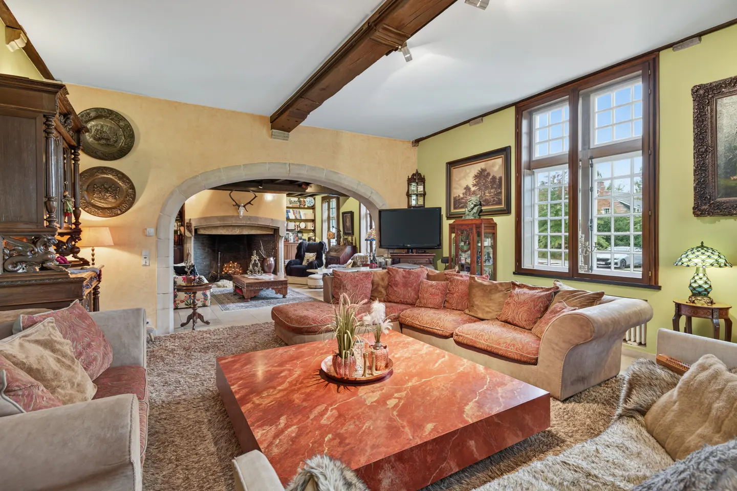 A living room with a large red marble coffee table, a fireplace, and a large window.
