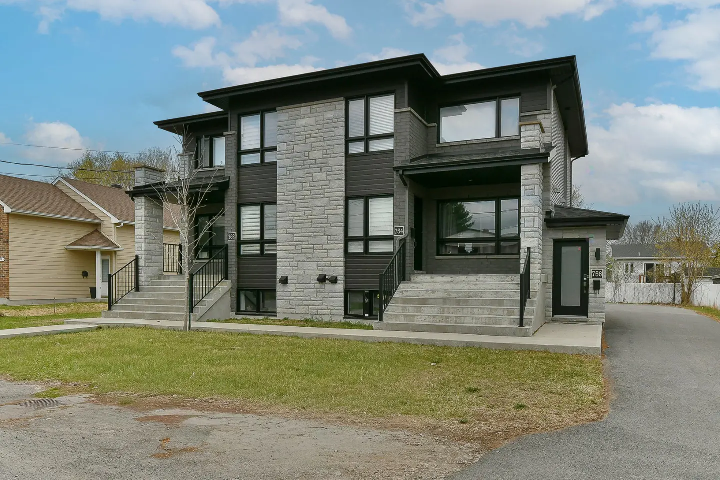 Modern two-story duplex with gray stone and dark siding, black framed windows, and concrete steps leading to each entrance.