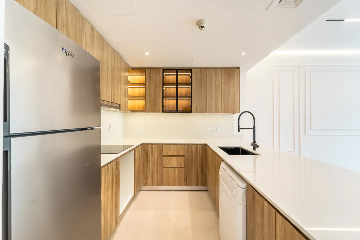 Bright kitchen with wood cabinets, white countertops, and stainless steel refrigerator. Black faucet and sink. White dishwasher.