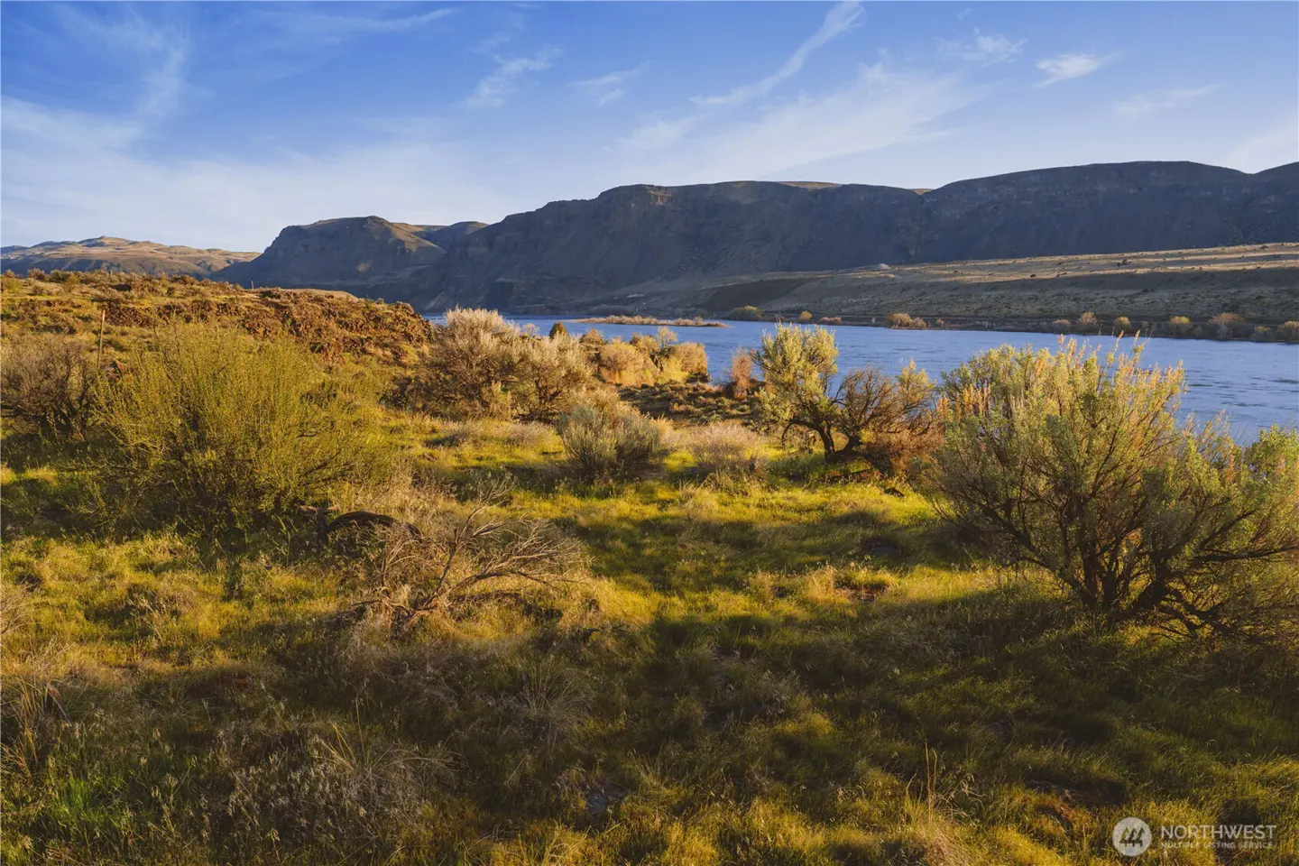 Scenic view of a blue river with grassy banks and mountains in the background under a blue sky.