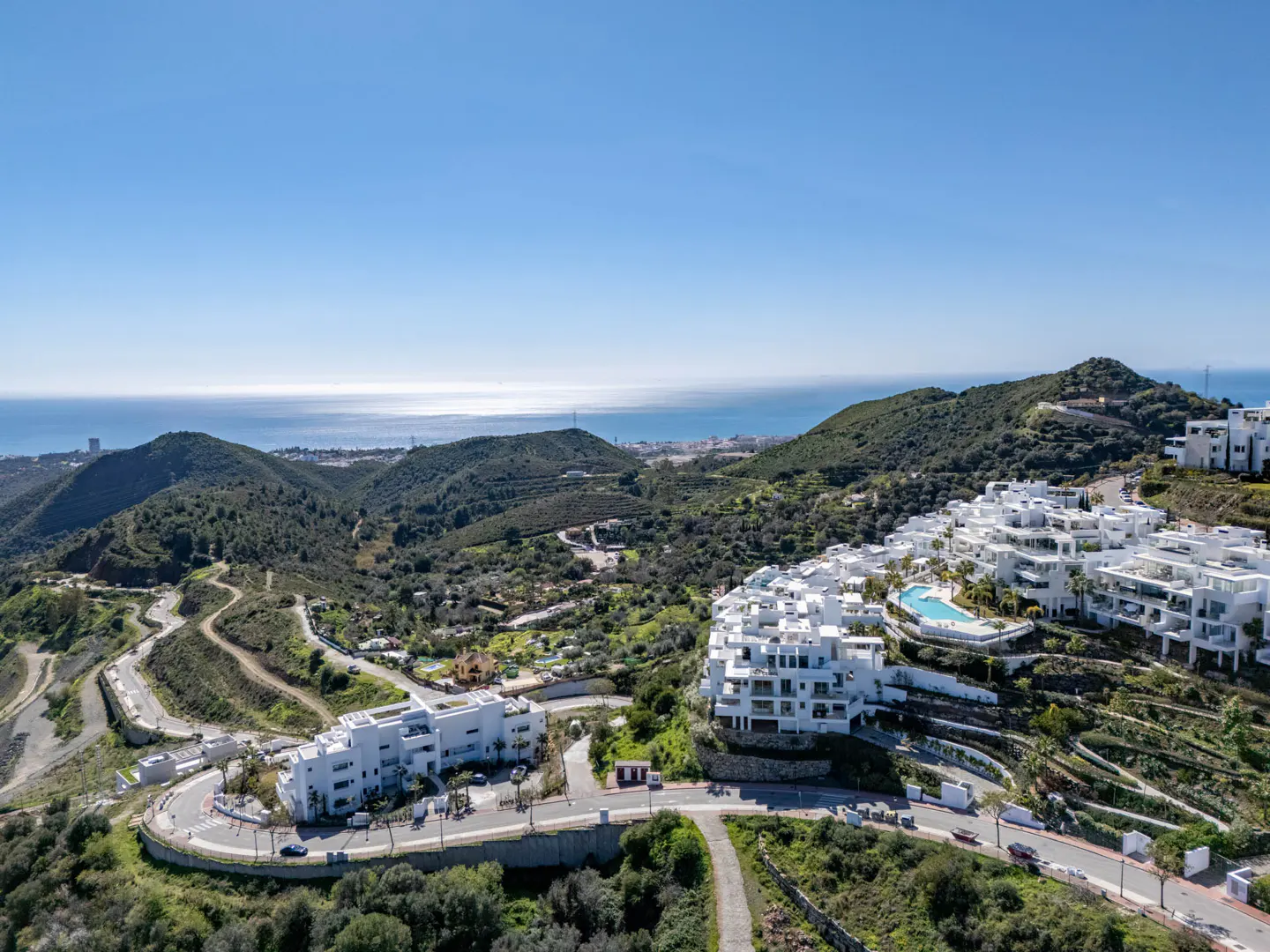 Scenic view of white condos nestled in green hills, under a blue sky, with the ocean visible in the distance.