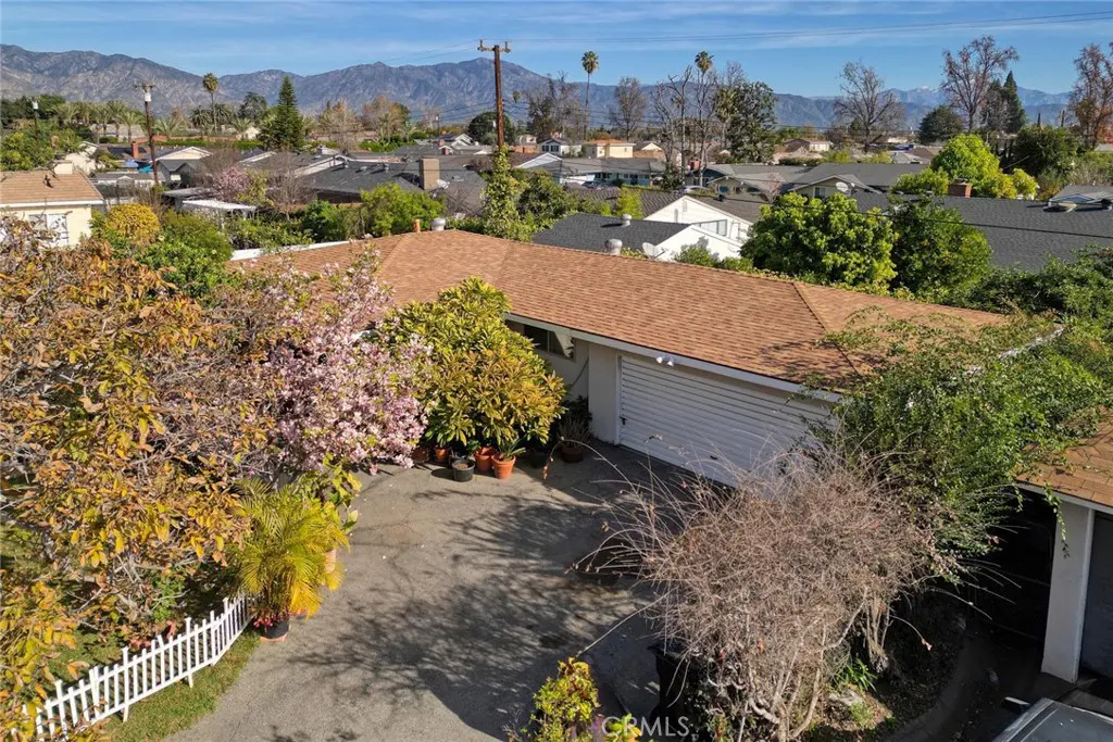 Aerial view of a single-story house with a brown roof, white garage door, and lush landscaping. Mountains are visible in the background.