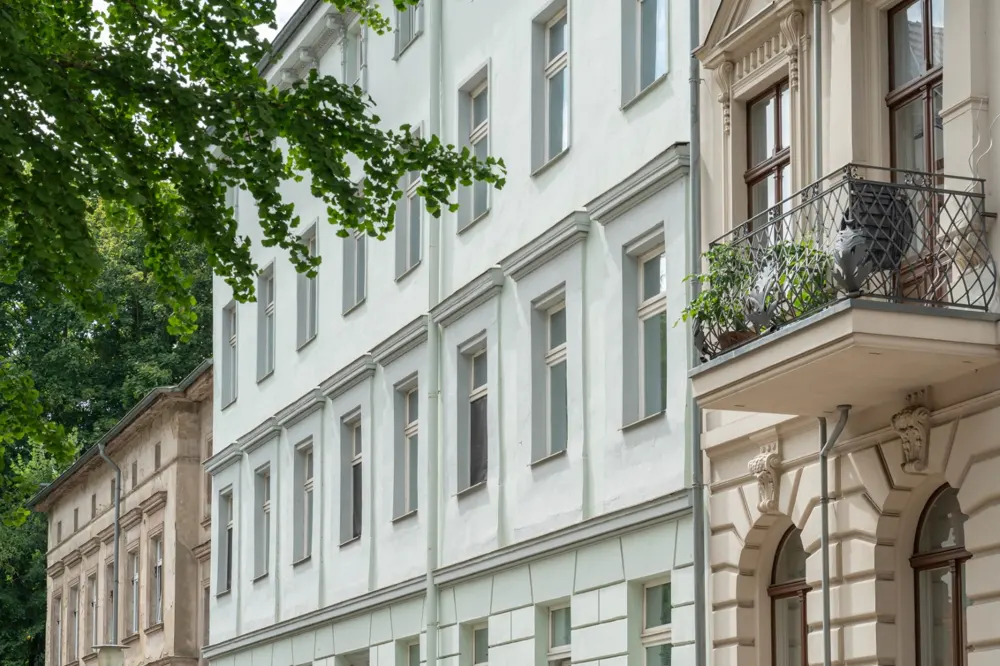 Exterior view of a light blue apartment building with a balcony and green trees.