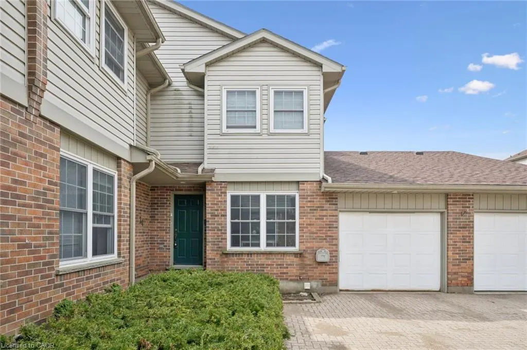Exterior view of a two-story townhouse with brick and beige siding, a green front door, and a white garage door.