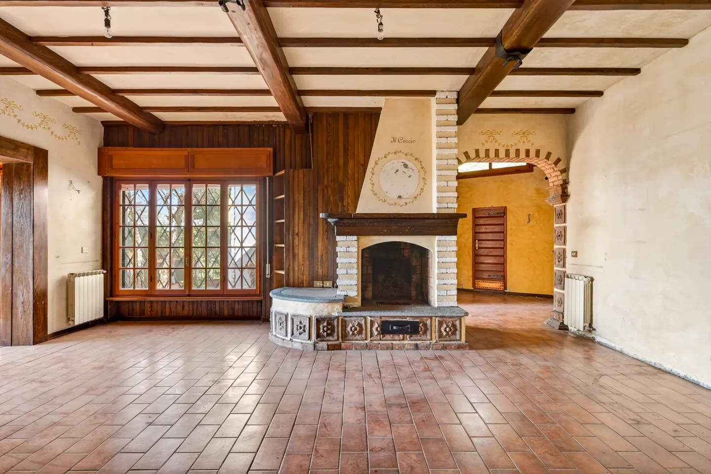 Unfurnished living room with brick floors, wood-paneled walls, and a large window. A fireplace with a decorative mantel is centered.