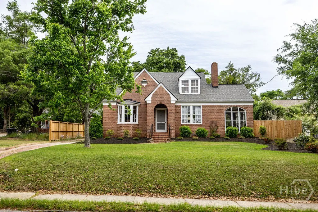 Brick house with gray roof, white trim, and green lawn. A large tree is on the left side of the house.