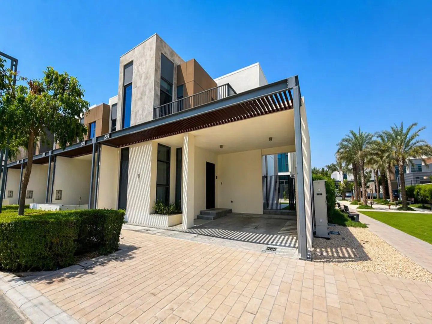 Modern townhouse with a covered parking area. The exterior features a mix of stone and white panels. Palm trees line the street.