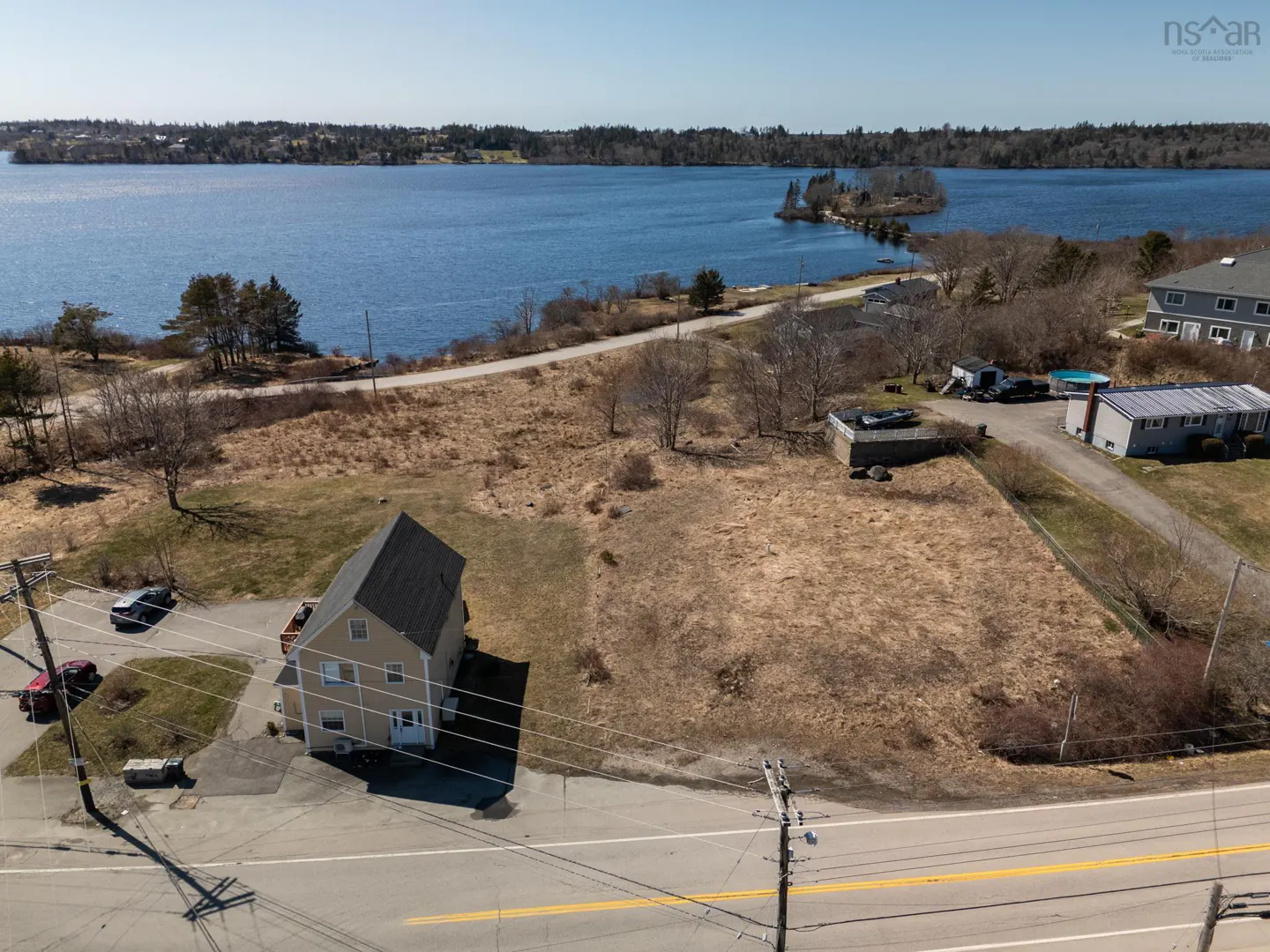 Aerial view of a tan two-story house with a black roof, cars in the driveway, and a blue lake in the background.