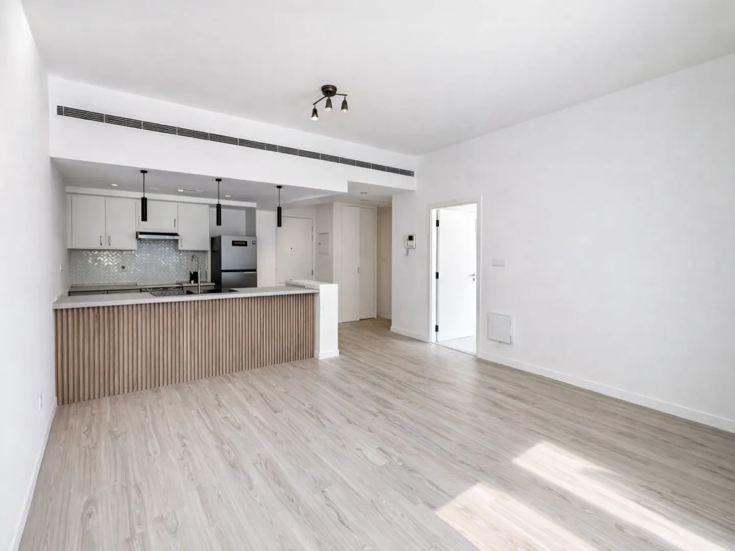 Modern open-plan kitchen with white cabinets, a wood-slat breakfast bar, and light wood flooring in a bright apartment.