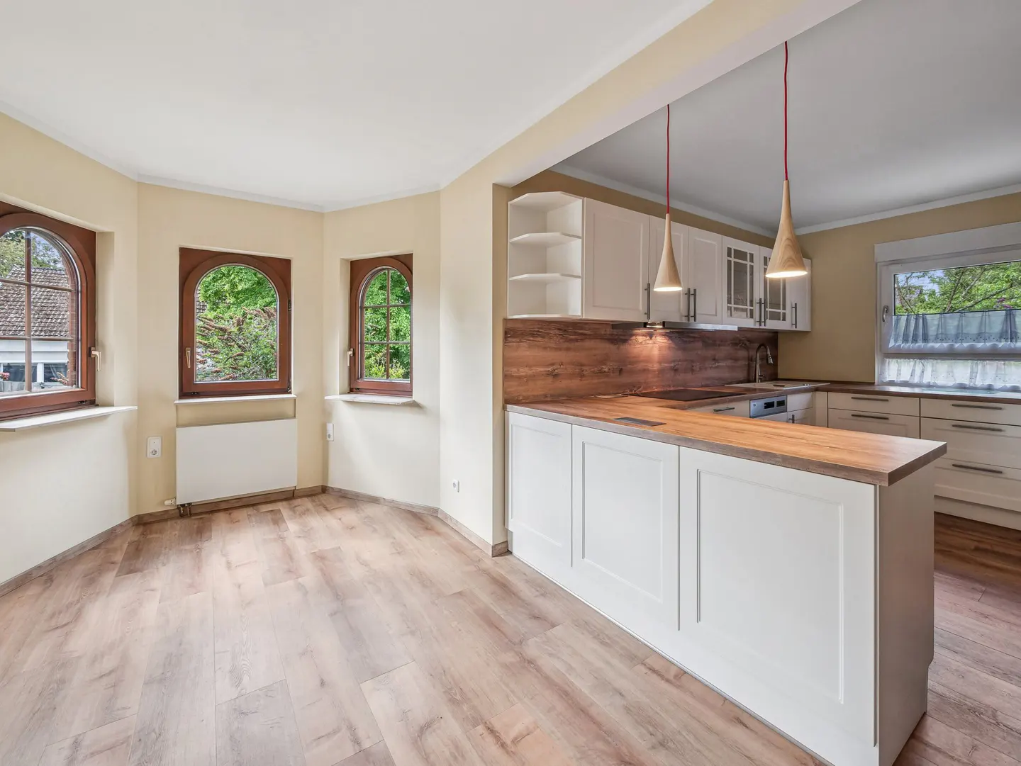 A bright, open kitchen with wood floors, white cabinets, and three arched windows. Two pendant lights hang over the island.