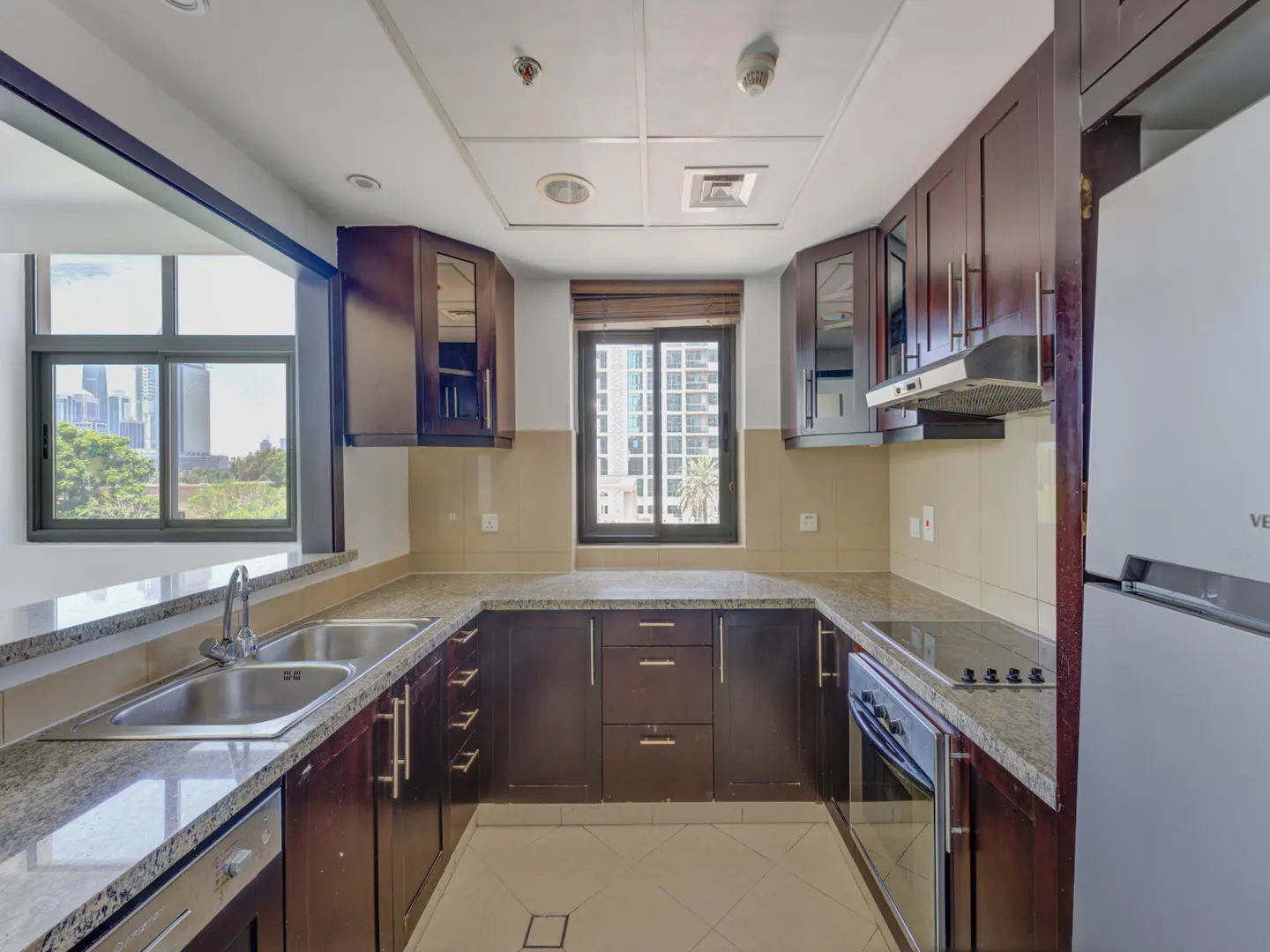 A U-shaped kitchen with dark wood cabinets, granite countertops, and stainless steel appliances. A window overlooks a city skyline.