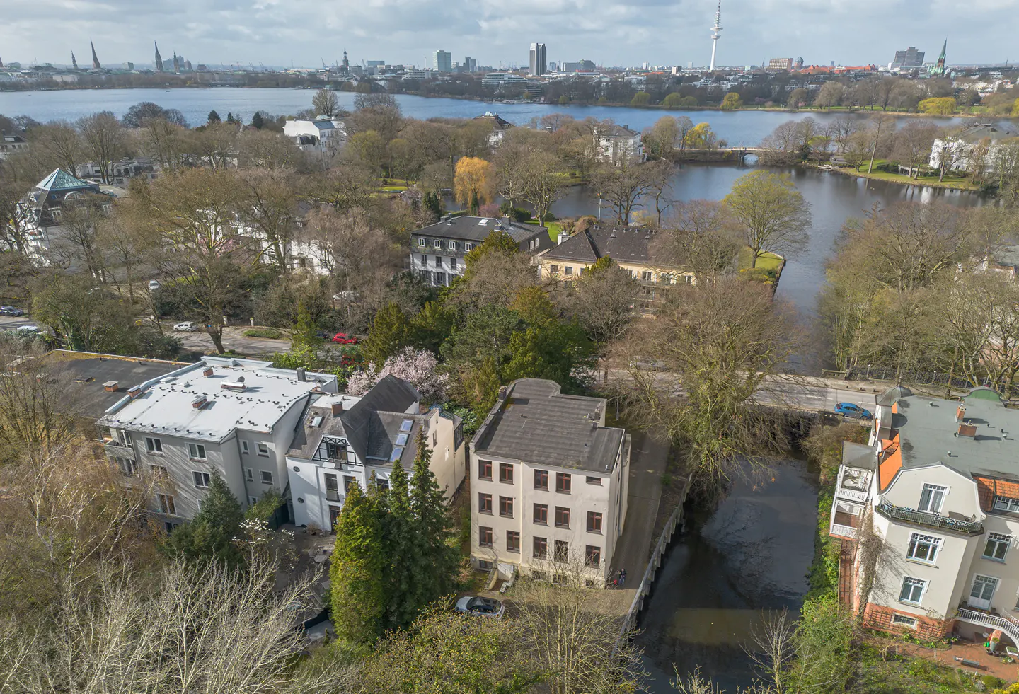 Aerial view of residential buildings near a canal and lake, with a distant city skyline under a bright blue sky.