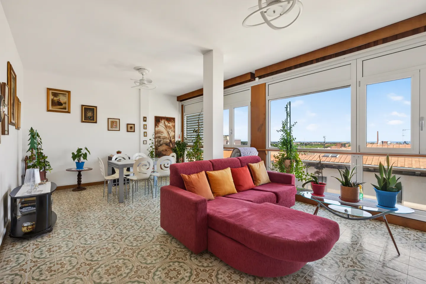 Bright living room with a red sectional sofa, patterned tile floors, dining area, and large windows with a scenic view.