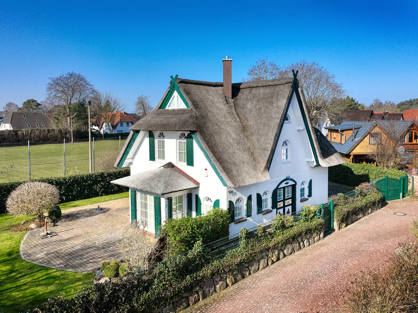 Exterior view of a white house with a thatched roof and green shutters on a sunny day.