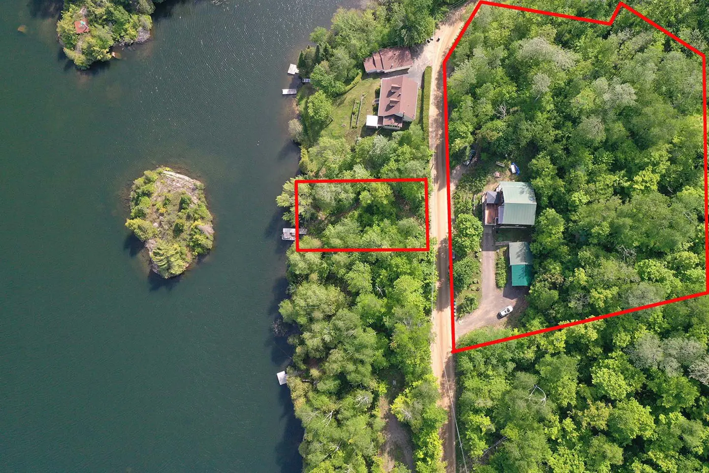 Aerial view of a wooded lakefront property with red outlines highlighting the house lot and a separate waterfront parcel.