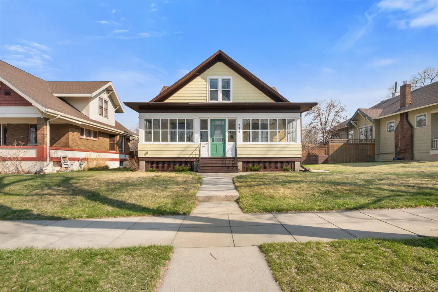 Exterior view of a yellow two-story house with a green door and a sunroom on a sunny day.