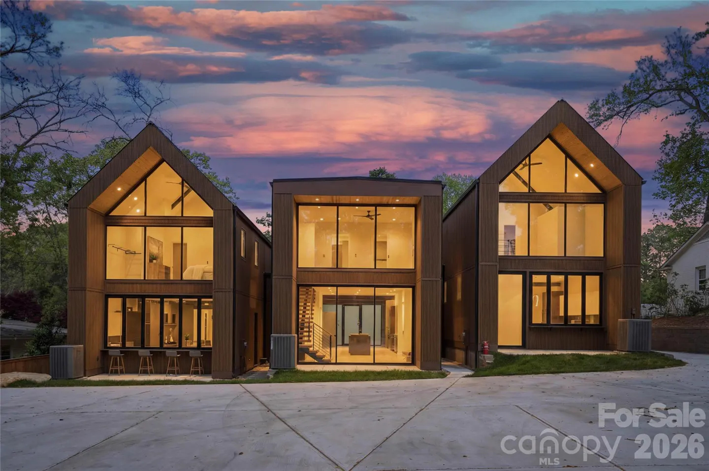 Modern three-story home with dark wood siding and floor-to-ceiling windows at dusk under a vibrant purple sunset.