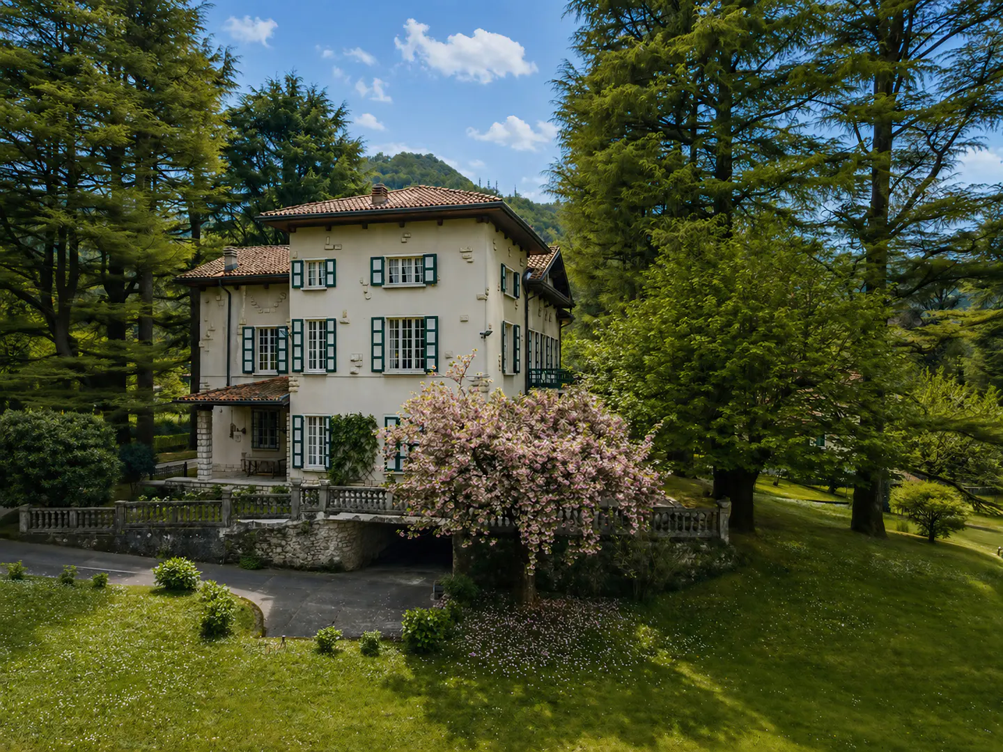 Elegant two-story house with white walls, green shutters, and a red tile roof, surrounded by lush green trees and lawn.