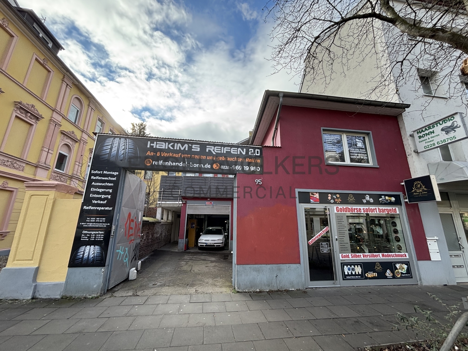 Commercial building with a tire shop, "Hakim's Reifen 2.0," and a gold exchange, "Goldbörse sofort bargeld," on a cloudy day.