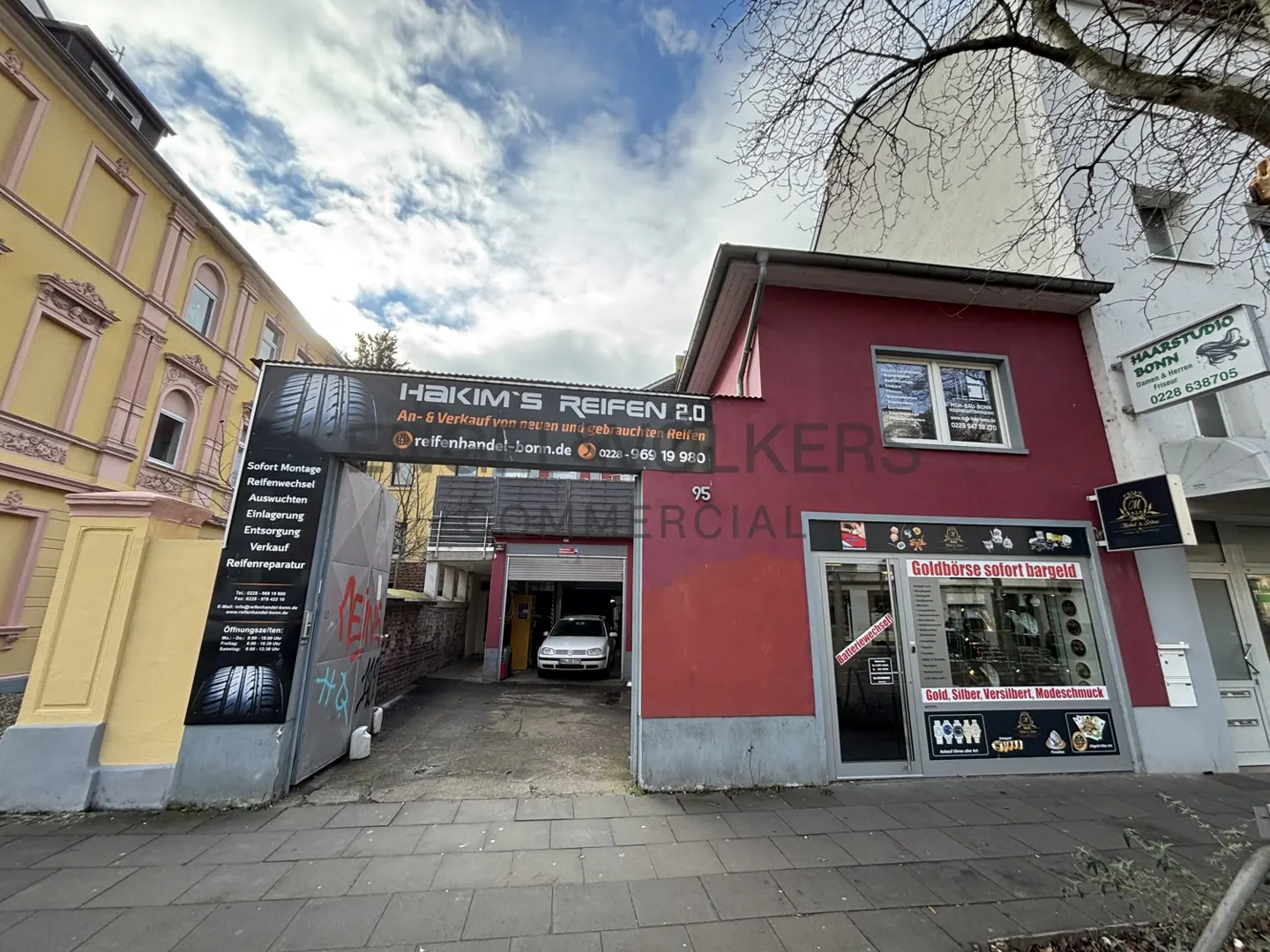 Commercial building with a tire shop, "Hakim's Reifen 2.0," and a gold exchange, "Goldbörse sofort bargeld," on a cloudy day.