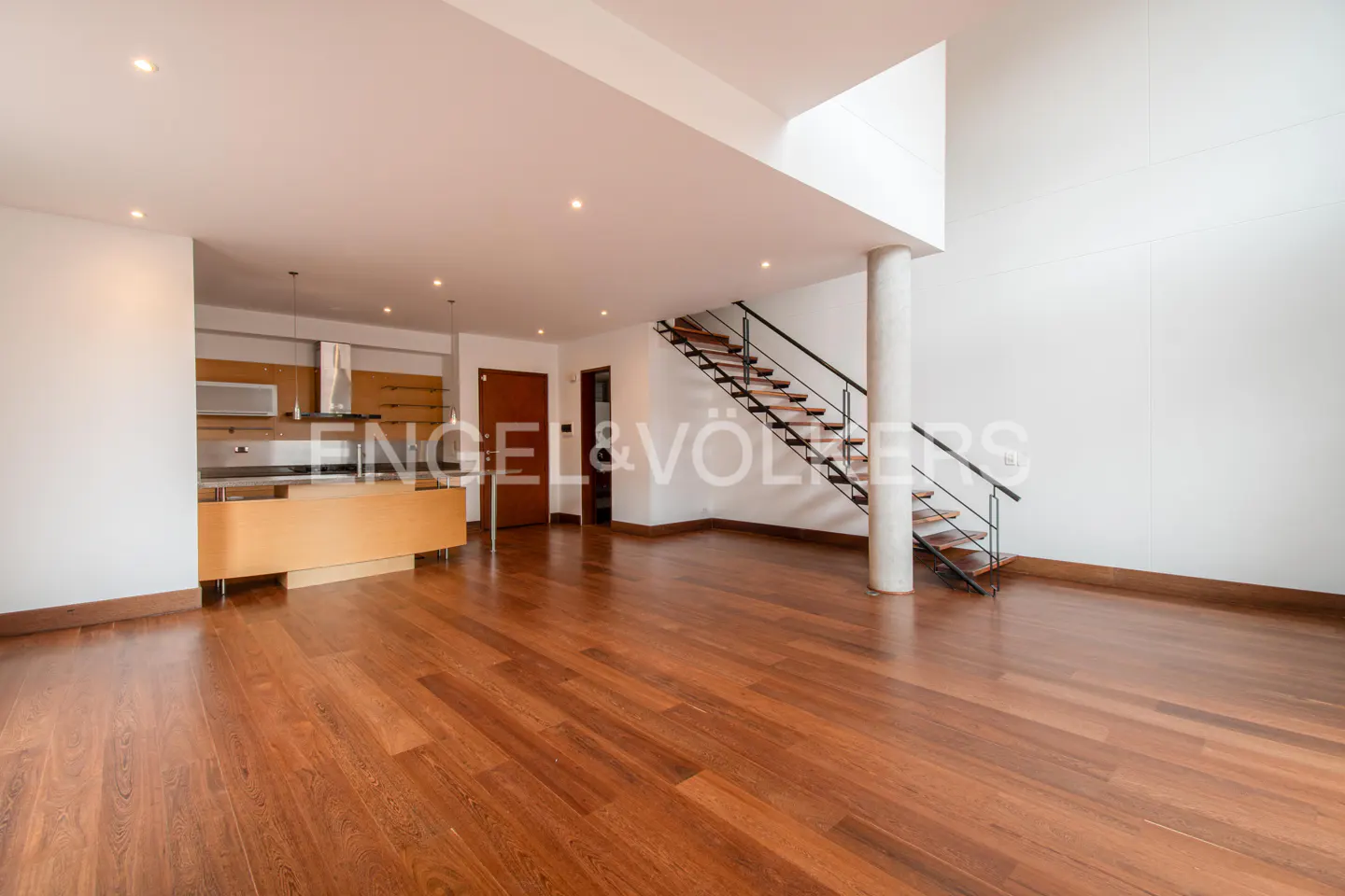 Bright, open-concept living space with hardwood floors, a modern kitchen, and a staircase leading to a second level.