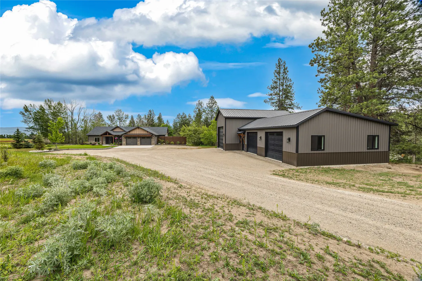 Exterior view of a gray house and garage with a gravel driveway on a sunny day.