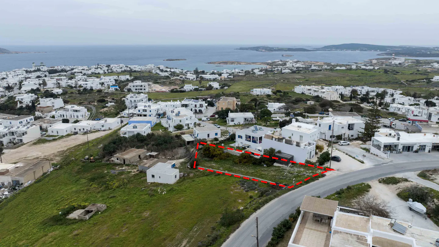 Aerial view of a property outlined in red, surrounded by white buildings, green hills, and the ocean in the background.